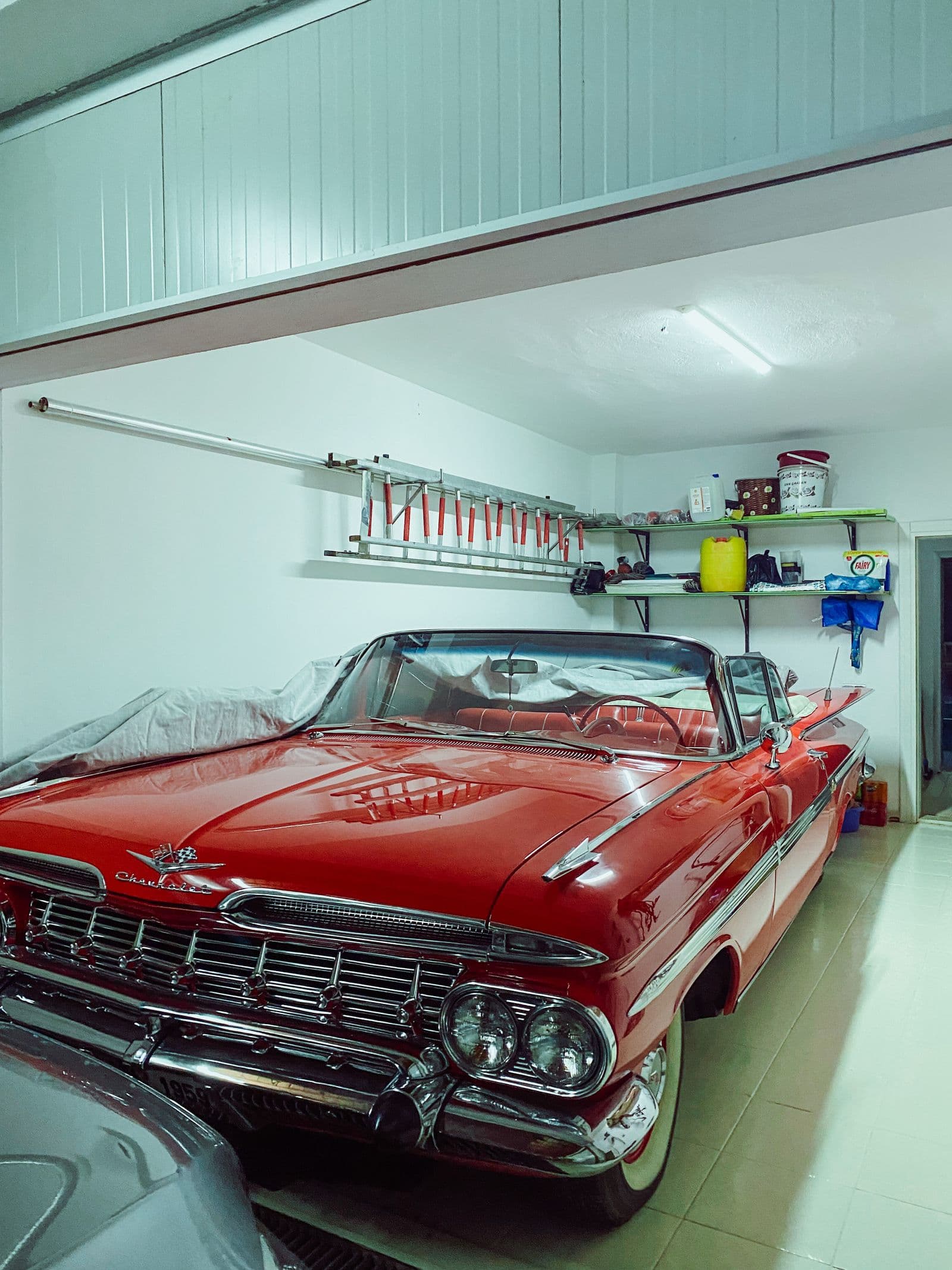 Clean residential garage with a light coated floor, storage shelves, and a classic car